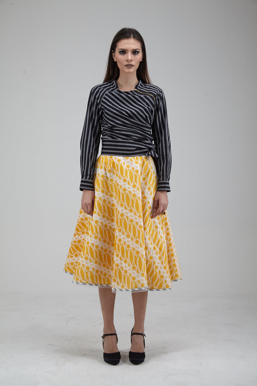 Woman wearing a black and white striped top with a yellow patterned skirt on a gray background